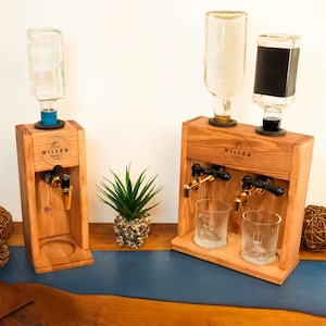 two wooden dispensers, each with a glass bottle and two glass cups, placed on a wooden surface.