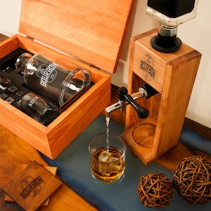 a wooden dispenser pouring a drink into a glass, with a wooden box containing additional glasses and a wooden coaster nearby.