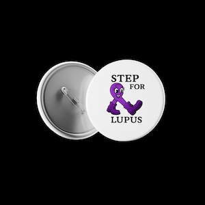 May include: A white button with a purple ribbon character wearing purple boots. The button reads "STEP FOR LUPUS" in black text. The back of the button is silver.