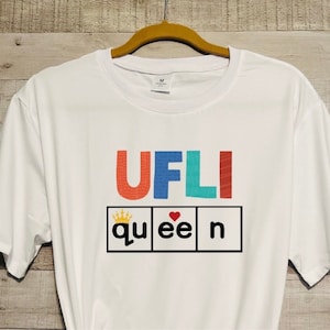 May include: White t-shirt with the text "UFLI queen" in colorful block letters. The word "queen" is in a box with a crown and a heart.