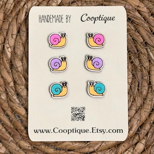 May include: A set of six snail-shaped earrings on a cream-colored card. Each snail has a yellow body and a shell in pink, purple, or teal. The card reads "HANDMADE BY Cooptique" and "www.Cooptique.Etsy.com".