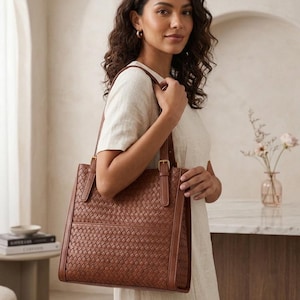 May include: A medium-sized brown tote bag featuring a woven leather exterior pattern, smooth leather side panels, and two adjustable shoulder straps with gold-toned metal buckles. The bag has a structured rectangular shape and a flat base.