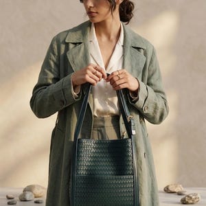 May include: A dark forest green tote bag featuring a woven leather exterior pattern, two vertical shoulder straps with gold-toned metal buckles, and a structured rectangular silhouette with a flat base and an open top design.