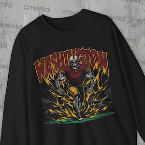 May include: Black sweatshirt featuring a graphic print of a football player wearing a helmet and running, with the word "WASHINGTON" in bold letters above him.