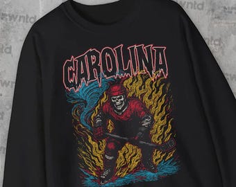 May include: Black sweatshirt featuring a hockey-playing skeleton in red and black gear, holding a hockey stick. The word "CAROLINA" is displayed in a red, stylized font above the skeleton, with flames and a blue swirl in the background.