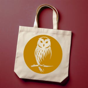 Op de afbeelding: Een witte canvas tote bag met een gele cirkel met een witte silhouet van een uil die op een tak zit.