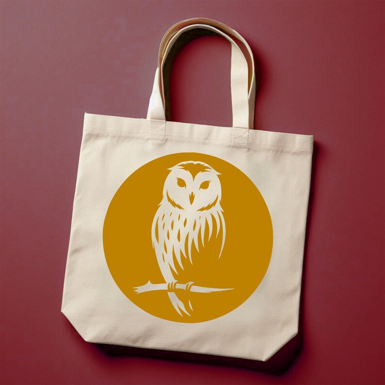 Op de afbeelding: Een witte canvas tote bag met een gele cirkel met een witte silhouet van een uil die op een tak zit.