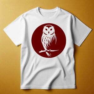 Op de afbeelding: Wit T-shirt met een rode cirkelvormige afbeelding van een witte uil die op een tak zit.