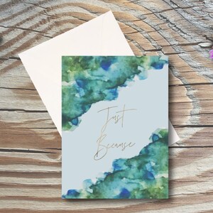 May include: A light blue card with a watercolor design in shades of green and blue. The text "Just Because" is written in gold script.