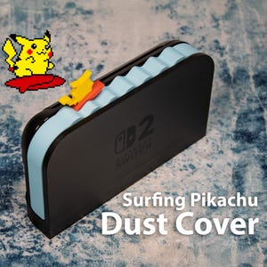 Pode incluir: Capa de pó preta para console Nintendo Switch, com um design de ondas azul claro e um gráfico de Pikachu surfando amarelo e vermelho. O texto "Surfing Pikachu Dust Cover" é exibido.