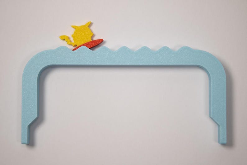 Peut inclure: Une pi&egrave;ce d&eacute;corative bleue clair, arqu&eacute;e, avec un dessus en forme de vagues. Une figurine jaune sur une planche de surf rouge est positionn&eacute;e sur les vagues. La pi&egrave;ce a une base rectangulaire.