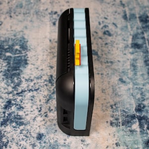 Peut inclure: Un appareil &eacute;lectronique noir et bleu clair avec un accent jaune. L'appareil a un design incurv&eacute; avec une bande bleu clair sur le c&ocirc;t&eacute;. Un petit &eacute;l&eacute;ment jaune est visible sur le c&ocirc;t&eacute; de l'appareil.