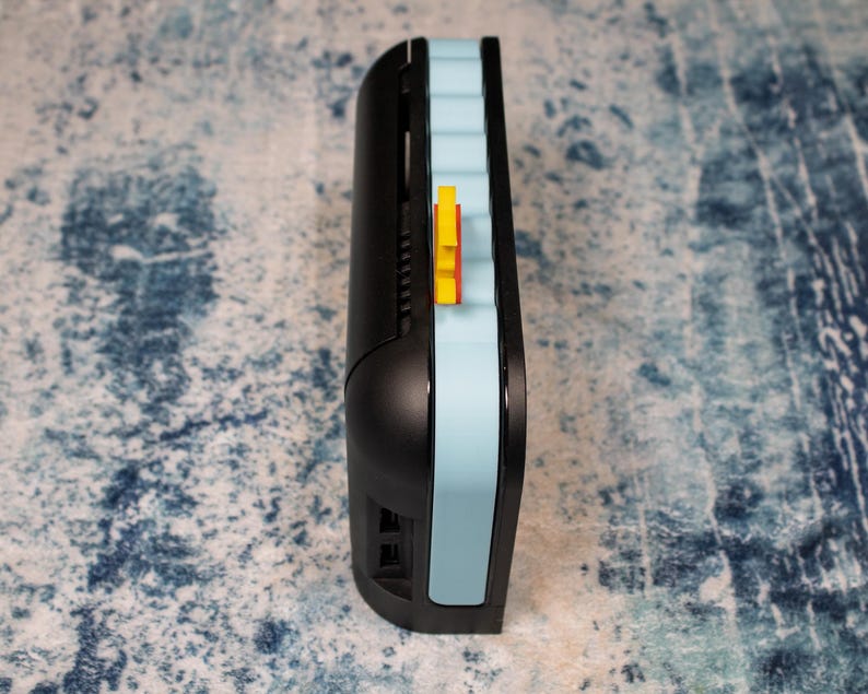 Peut inclure: Un appareil &eacute;lectronique noir et bleu clair avec un accent jaune. L'appareil a un design incurv&eacute; avec une bande bleu clair sur le c&ocirc;t&eacute;. Un petit &eacute;l&eacute;ment jaune est visible sur le c&ocirc;t&eacute; de l'appareil.