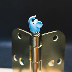 Könnte beinhalten: Ein goldenes Türscharnier mit einer blauen Elefantenfigur darauf.