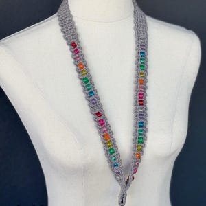 May include: A gray knitted lanyard with a rainbow of colorful beads. The lanyard has a silver-colored clasp at the bottom and is displayed on a mannequin. The text "fox creations" is visible at the bottom.