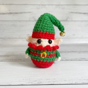 May include: A handmade crochet elf doll with a green hat, red trim, and a green and red outfit. The elf has black eyes, rosy cheeks, and a small gold bell on the hat. A charming holiday decoration.
