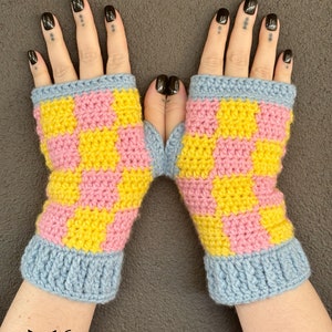 Könnte beinhalten: Ein Paar handgefertigte Fingerhandschuhe. Die Handschuhe haben ein gelb-rosa Schachbrettmuster mit hellblauen Bündchen. Die Handschuhe sind aus weichem Strickmaterial gefertigt. Das Fox Creations-Logo befindet sich unten links.