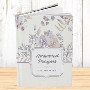 Puede incluir: Un diario blanco con un diseño floral y el texto "Answered Prayers and Miracles" en la portada.