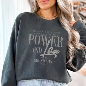 May include: A dark gray sweatshirt with a white graphic print that reads "For God has not given us a spirit of fear, but of power and love and of a sound mind 2 Timothy 1:7".