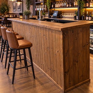 May include: A wooden bar counter with vertical plank paneling and a thick top edge, accompanied by a row of brown upholstered bar stools featuring black metal frames and footrests, positioned in a commercial space with a back bar display.