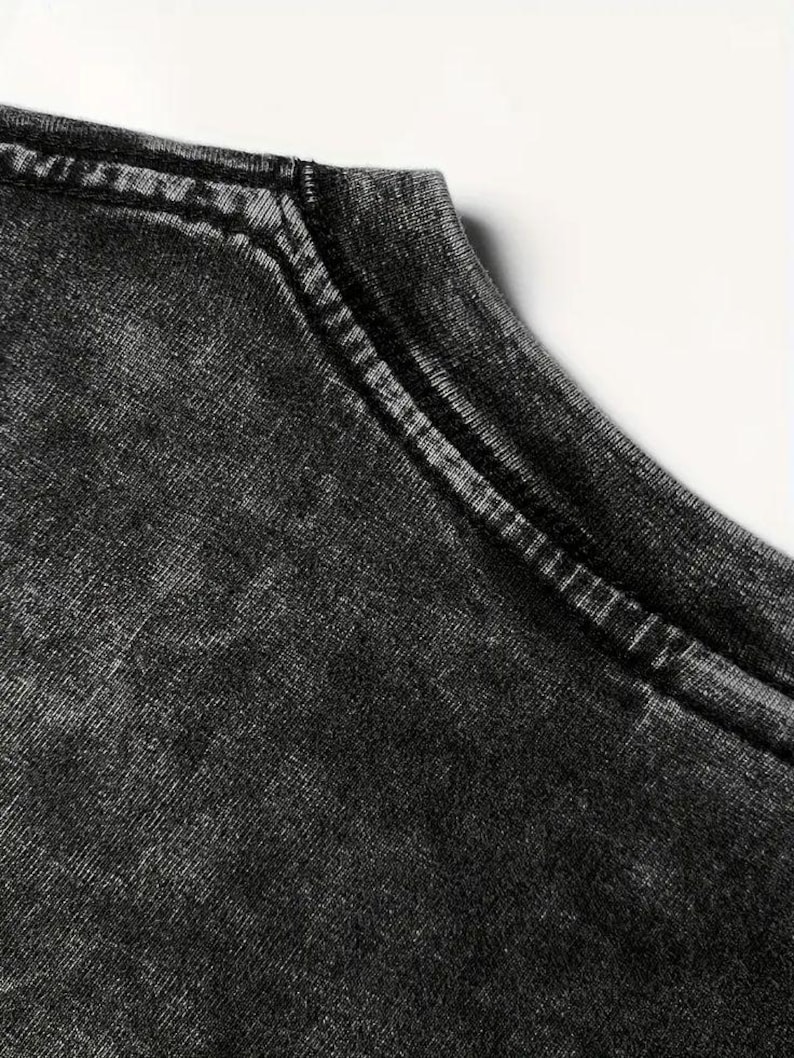 May include: Close-up of the neckline of a black t-shirt with a distressed, faded look. The fabric has a textured, worn appearance.