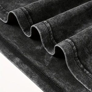 May include: Close-up of the black fabric edge of a garment, showing the stitching detail. The fabric has a distressed, vintage look.