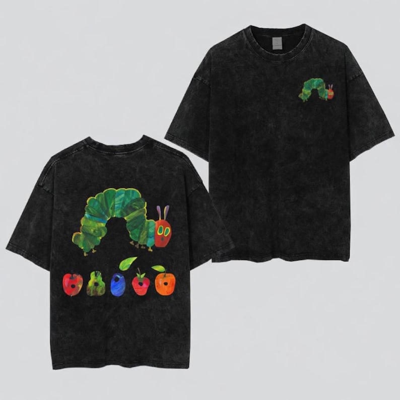 May include: A black acid-wash t-shirt featuring a small green caterpillar graphic on the front chest. The back of the shirt displays a large illustration of the same green caterpillar positioned above a row of five colorful fruits including an apple.