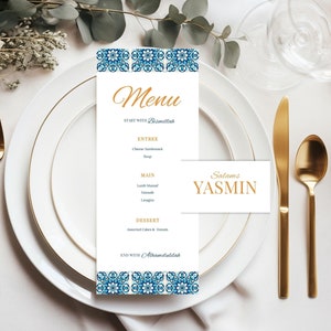 Könnte beinhalten: Eine weiße Speisekarte mit einem blauen und weißen Muster an der Kante. Die Speisekarte listet die Gerichte auf, die bei einem Hochzeitsessen serviert werden, darunter "Lanh Mansal", "Fatoush" und "Lasagna". Die Karte enthält auch den Text "Salams Yasmin" in goldenen Buchstaben.