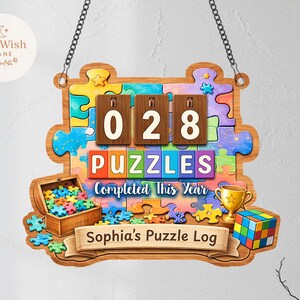 Puede incluir: Letrero de madera con forma de rompecabezas con el texto "028 PUZZLES Completed this Year". Presenta un cofre del tesoro con piezas de rompecabezas, un trofeo y un cubo de Rubik. Incluye el texto "Sophia's Puzzle Log".