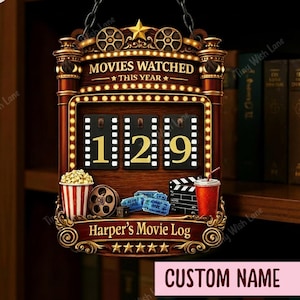 Könnte beinhalten: Hölzernes Filmlog-Schild mit dem Text "MOVIES WATCHED THIS YEAR" und der Zahl "129". Das Schild enthält einen Popcorn-Eimer, eine Filmrolle, Kinokarten, eine Filmklappe und ein Getränk. Das Schild ist personalisierbar.