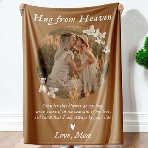 May include: A brown fleece blanket with a photo of a mother and daughter hugging. The blanket has the text "Hug from Heaven" at the top and "Consider this blanket as my hug, wrap yourself in the warmth of my love, and know that I am always by your side. Love, Mom" at the bottom.