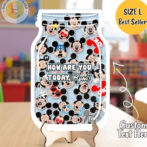 May include: A jar-shaped decorative item featuring various Mickey Mouse expressions on a light blue background. The item includes the text "How are you today, Ryan?" and is displayed on a wooden stand. A yellow circle indicates "Size L Best Seller."