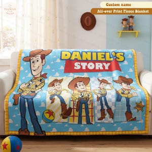 Może przedstawiać: Niebieski polarowy koc z postacią Chudego z Toy Story. Koc ma napis "DANIEL'S STORY" i powtarzający się wz&oacute;r Chudego w r&oacute;żnych pozach. Koc leży na białej kanapie.