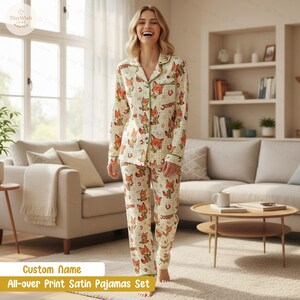 Puede incluir: Conjunto de pijama de sat&eacute;n color crema con un estampado integral de zorros de dibujos animados en naranja y marr&oacute;n. El pijama tiene ribetes verdes y el texto "Joseph" es visible. El conjunto incluye una camisa con botones y pantalones a juego.