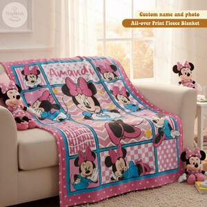 May include: A pink fleece blanket with a Minnie Mouse design, featuring the name "Amandi". The blanket displays multiple images of Minnie Mouse and the word "MINNIE" in a grid pattern. The blanket is draped over a white sofa.