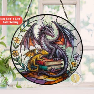 Może przedstawiać: Wisiorek z witrażu przedstawia dwa smoki, jeden fioletowy, a drugi żółty, siedzące na stosie książek. Smoki otoczone są kwiatami i winoroślą. Wisiorek ma średnicę 9,84 cala.