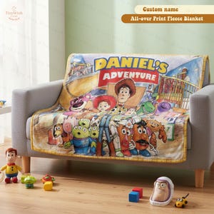 May include: A fleece blanket featuring a colorful graphic print of various animated toy characters, including a cowboy, a cowgirl, and aliens. The text "DANIEL'S ADVENTURE" is printed in large yellow and red letters across the top of the blanket.