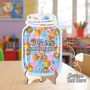 Op de afbeelding: Een lichtblauwe houten beloningskaart in de vorm van een pot met de tekst "Oliver's Elemental Rewards!" en diverse cartoonkaraktertokens. De pot wordt op een houten standaard tentoongesteld.