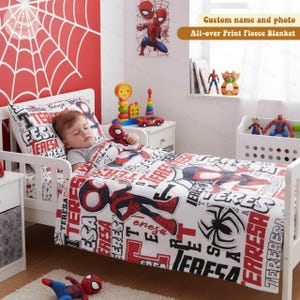 Może przedstawiać: Ł&oacute;żko dziecięce z białą ramą, z kołdrą, poszewką na poduszkę i grafiką ścienną w stylu Spider-Mana. Pościel jest biała z czerwono-czarną grafiką i tekstem Spider-Mana. Pluszowa zabawka Spider-Man spoczywa na ł&oacute;żku.