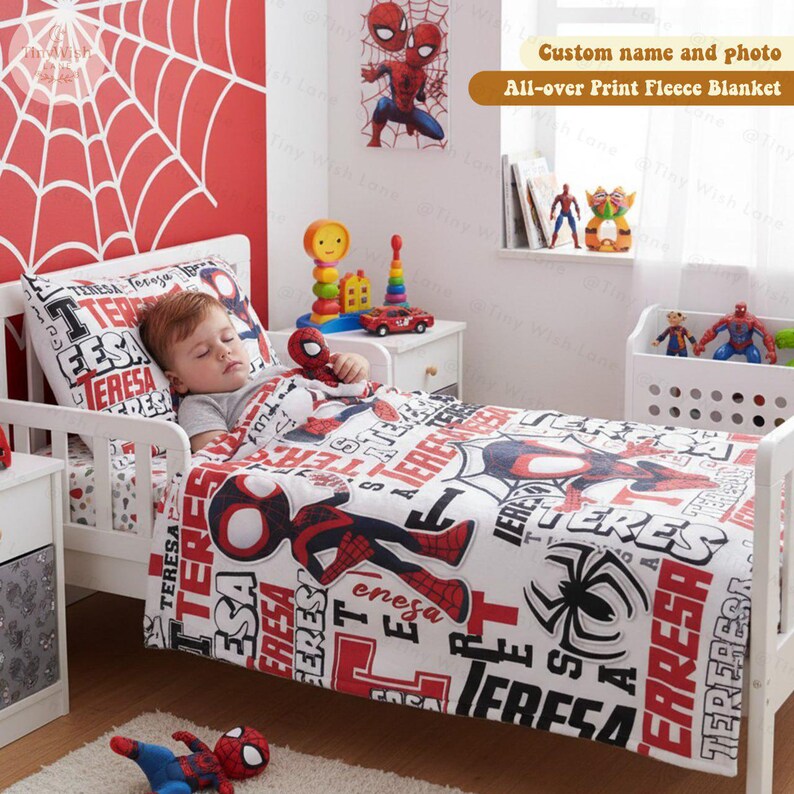 Może przedstawiać: Ł&oacute;żko dziecięce z białą ramą, z kołdrą, poszewką na poduszkę i grafiką ścienną w stylu Spider-Mana. Pościel jest biała z czerwono-czarną grafiką i tekstem Spider-Mana. Pluszowa zabawka Spider-Man spoczywa na ł&oacute;żku.