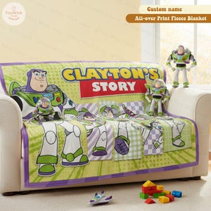 Może przedstawiać: Zielony, biały i fioletowy polar z wzorem Buzza Astrala, z napisem "CLAYTON'S STORY". Kocyk jest narzucony na sofę, w pobliżu znajdują się figurki i zabawki Buzza Astrala. Kocyk ma szerokość około 152 cm.