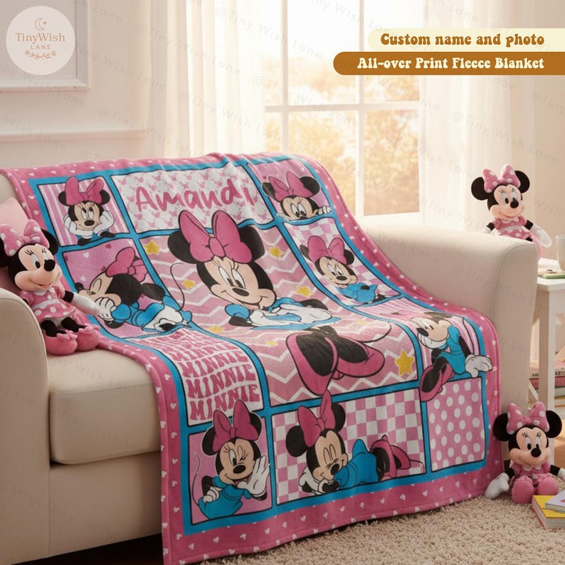 Może przedstawiać: R&oacute;żowy polar z Minnie Mouse, z imieniem "Amandi". Kocyk przedstawia wiele obraz&oacute;w Minnie Mouse i słowo "MINNIE" w wzorze kratki. Kocyk leży na białej sofie.