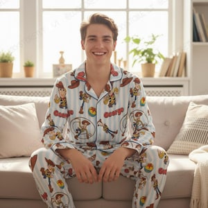 Puede incluir: Un conjunto de pijama de camisa de manga larga con botones y pantalón a juego, con un patrón de rayas verticales en azul claro y blanco. La tela está decorada con un estampado repetitivo del personaje Woody de Toy Story, sombreros y pelotas.