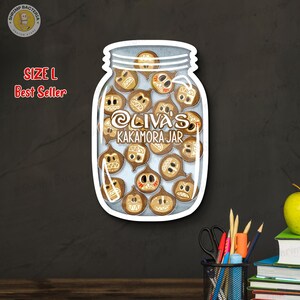 May include: A sticker in the shape of a jar filled with cartoonish brown coconuts with various facial expressions. The jar has the text "Oliva's Kakamora Jar" and "Size L Best Seller". The sticker has a white border and is on a dark background.