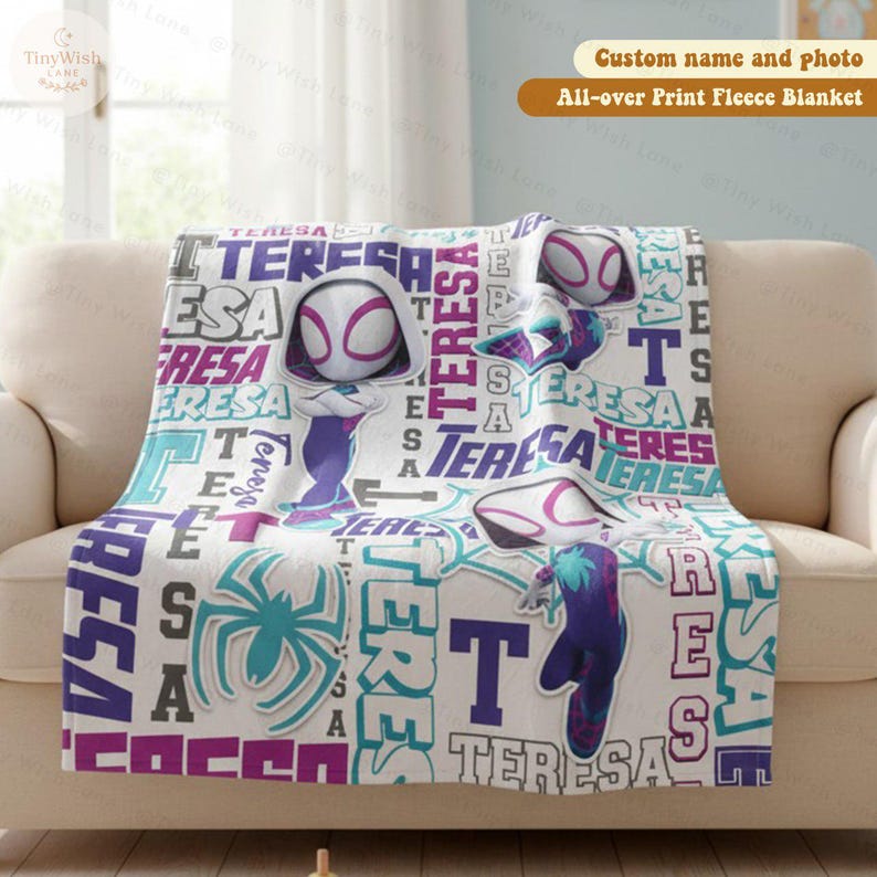 Może przedstawiać: Biały koc z polaru z nadrukiem na całej powierzchni przedstawiającym superbohaterkę. Koc zawiera imię "TERESA" w r&oacute;żnych czcionkach i kolorach, a także obrazy superbohater&oacute;w. Koc jest prezentowany na beżowej sofie.