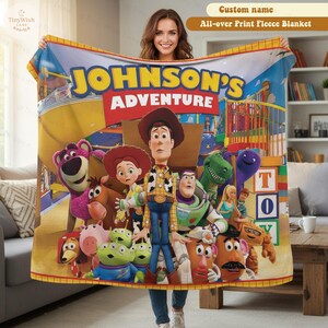 May include: A fleece blanket featuring a colorful Toy Story character print with the text JOHNSON'S ADVENTURE. The design includes Woody, Buzz Lightyear, Jessie, Rex, Slinky Dog, Hamm, Mr. Potato Head, Lotso, and the Aliens on a playground background.