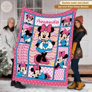 Może przedstawiać: R&oacute;żowy koc z polaru z Minnie Mouse w r&oacute;żnych pozach. Koc ma powtarzający się wz&oacute;r z wizerunkami Minnie Mouse, tło w zygzaki i imię "Amanda" pośrodku. Koc jest obszyty r&oacute;żową obw&oacute;dką i niebieskimi akcentami.