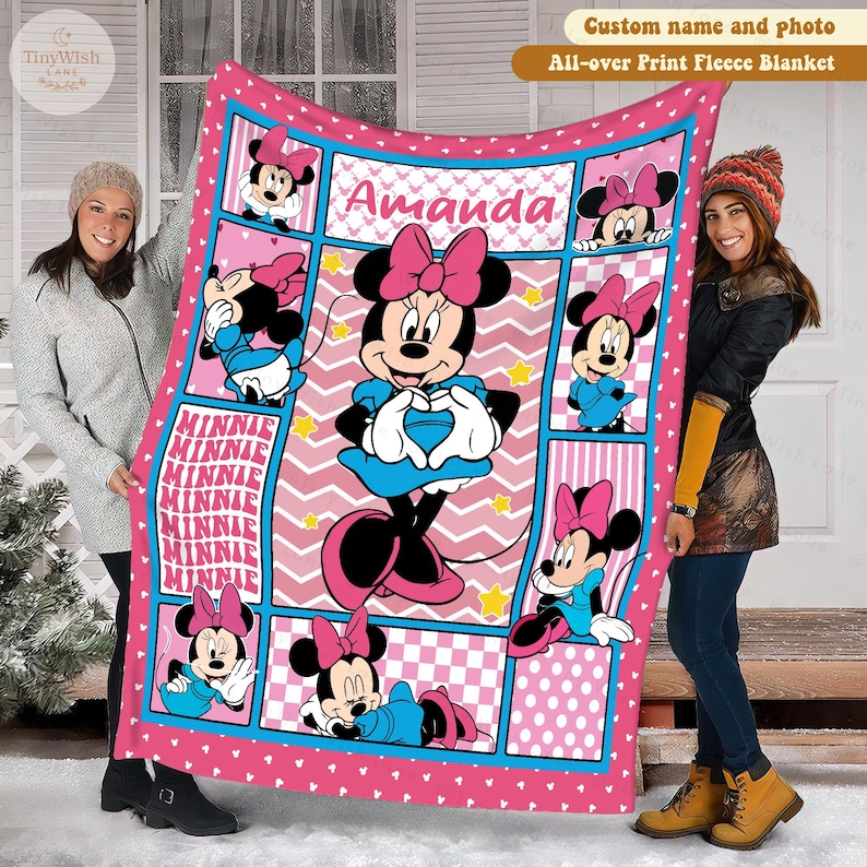 Może przedstawiać: R&oacute;żowy koc z polaru z Minnie Mouse w r&oacute;żnych pozach. Koc ma powtarzający się wz&oacute;r z wizerunkami Minnie Mouse, tło w zygzaki i imię "Amanda" pośrodku. Koc jest obszyty r&oacute;żową obw&oacute;dką i niebieskimi akcentami.