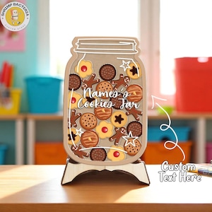 Puede incluir: Un letrero de madera con forma de tarro de galletas con varios diseños de galletas y el texto "Name's Cookies Jar". El letrero está sobre un soporte de madera. Las galletas son de varias formas y colores, incluyendo hombres de jengibre y estrellas.