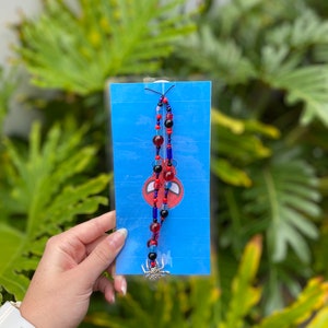May include: A blue card with a red and blue beaded keychain with a silver spider charm. The card has a cartoon image of Spider-Man on it.